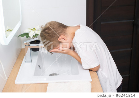 The cute boy leaned over to the sink to wash his face 96241814
