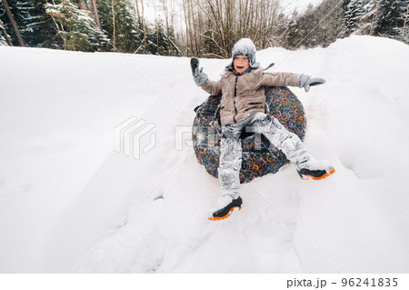 A boy is sitting in a tubing in the snow and riding down a slide A boy is sitting in a tubing in the snow and riding down a slide 96241835