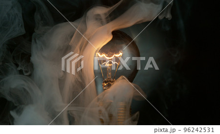 Close-up of shining light bulb with smoke, dark background 96242531