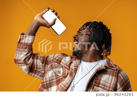 African guy in headphones singing song while listening music on smartphone on yellow background African guy in headphones singing song while listening music on smartphone on yellow background 96243263