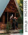 A happy family at a wooden house in the forest. A happy young couple with a child at the cottage. A young family. A young family is vacationing outside the city. Copy space 96244606