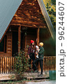 A happy family at a wooden house in the forest. A happy young couple with a child at the cottage. A young family. A young family is vacationing outside the city. Copy space 96244607