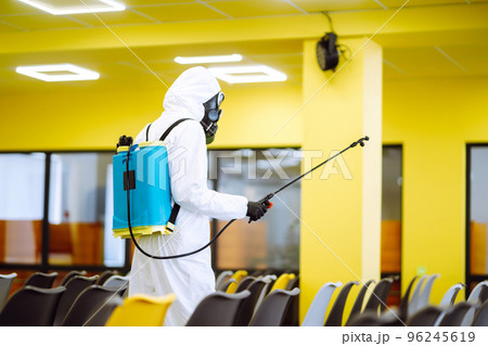 Man wearing protective suit disinfecting assembly hall with spray. Disinfecting of office. COVID-19. Man wearing protective suit disinfecting assembly hall with spray. Disinfecting of office. COVID-19. 96245619