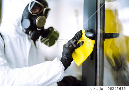 Man in protective hazmat suit washes door handles in office to preventing the spread of coronavirus. Man in protective hazmat suit washes door handles in office to preventing the spread of coronavirus. 96245636