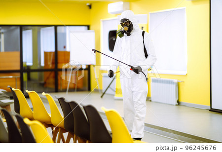 Man wearing protective suit disinfecting assembly hall with spray. Disinfecting of office. COVID-19. 96245676