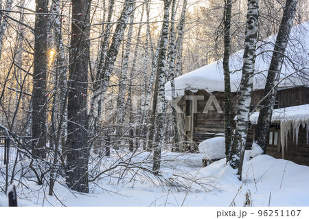 Old wooden house and stable with icicles on roof in birch snow-covered forest in winter at sunset Old wooden house and stable with icicles on roof in birch snow-covered forest in winter at sunset 96251107