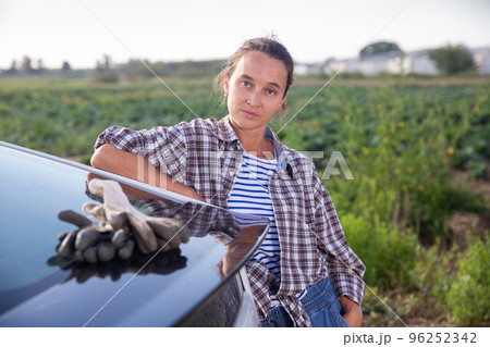 Confident female farmer standing near vehicle on farm field 96252342