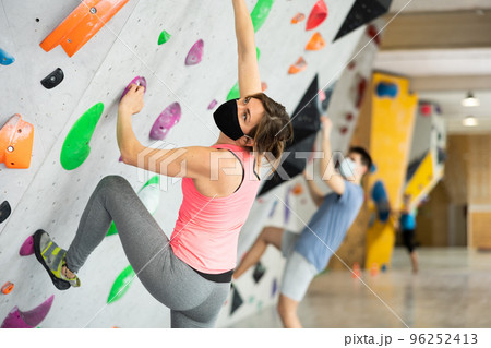 Caucasian woman in face mask exercising on wall in climbing gym during bouldering training. Caucasian woman in face mask exercising on wall in climbing gym during bouldering training. 96252413