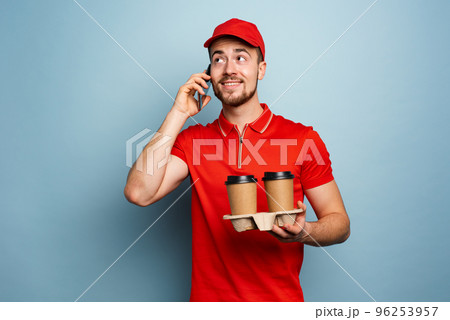 Courier delivers hot coffee and receive call on phone. Cyan background 96253957