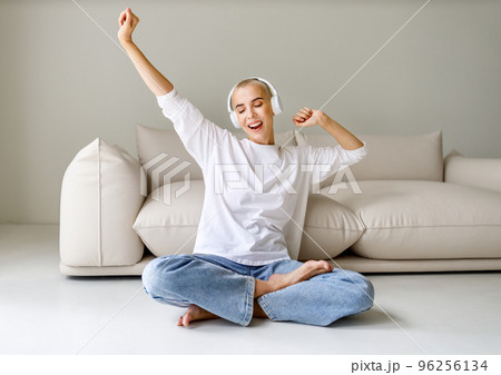 Beautiful woman meloman with very short hair listens to music and sings near couch 96256134