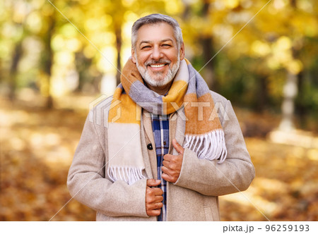 Happy positive mature man with broad smile in elegant clothes on an autumn walk in city park 96259193