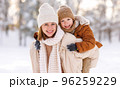 Mom giving piggyback ride to happy little son while walking outdoors in snowy winter park 96259229