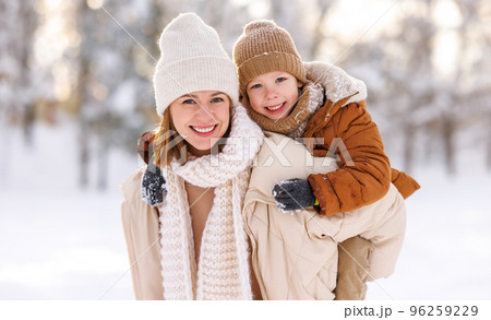 Mom giving piggyback ride to happy little son while walking outdoors in snowy winter park Mom giving piggyback ride to happy little son while walking outdoors in snowy winter park 96259229