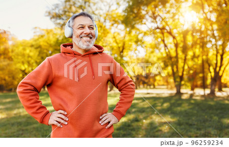 Happy positive mature man with broad in headphones smile while doing sport in city park Happy positive mature man with broad in headphones smile while doing sport in city park 96259234