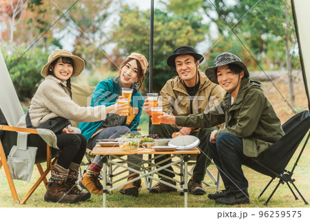仲間と一緒にキャンプ場でビールで乾杯するアジア人の男女（カメラ目線） 96259575