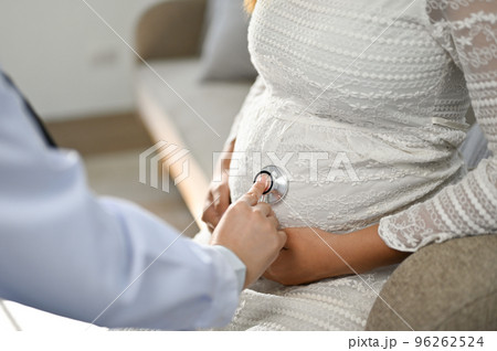 Female doctor using a stethoscope to listen to the baby's heartbeat in a pregnant woman's belly. 96262524