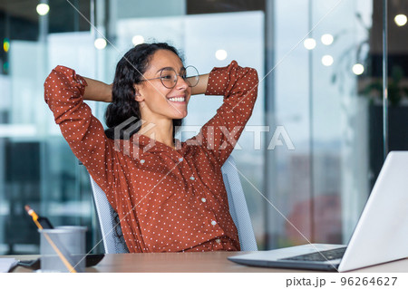 Satisfied happy and successful business woman smiling and resting, hispanic female worker finished work and put her hands behind her head, dreams of victory. Satisfied happy and successful business woman smiling and resting, hispanic female worker finished work and put her hands behind her head, dreams of victory. 96264627