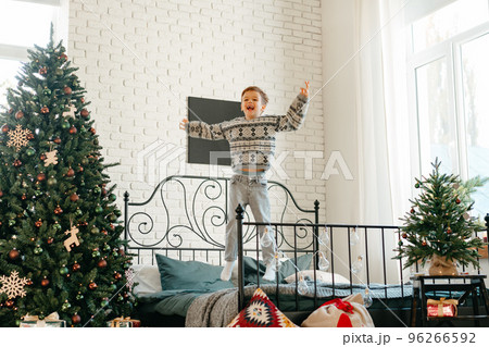 Little boy jumping on bed near Christmas tree Little boy jumping on bed near Christmas tree 96266592