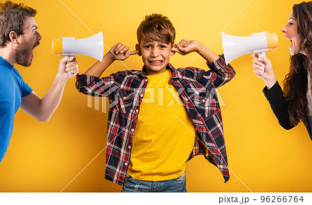 Child covers his ears because he does not want to hear the cries and reproaches of his parents. Yellow background 96266764