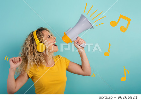 Woman sings with loudspeaker and listen to music with headset. joyful expression. cyan background 96266821