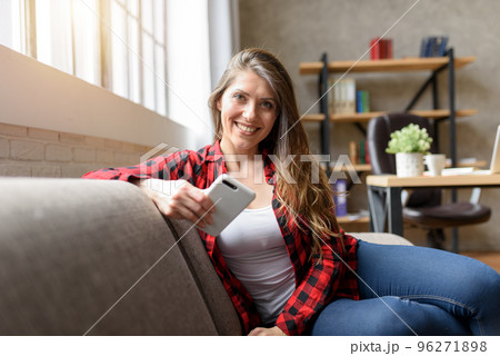 Smiling girl relaxing on a sofa with her smartphone 96271898