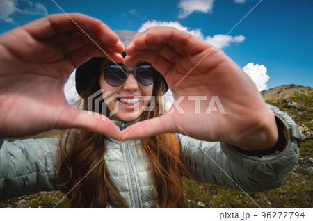 smiling young woman showing fingers gesture sign of heart, love in mountains, happy tourist 96272794