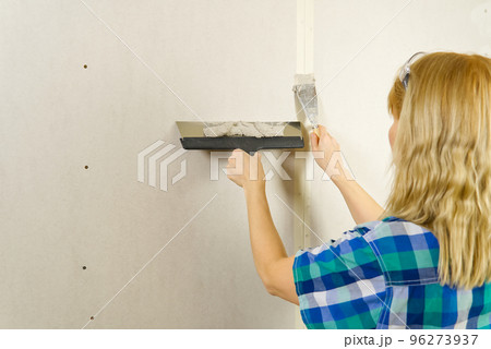 Woman putty plaster. Builder female indoor worker plastering wall with spatula trowel tool. Woman putty plaster. Builder female indoor worker plastering wall with spatula trowel tool. 96273937