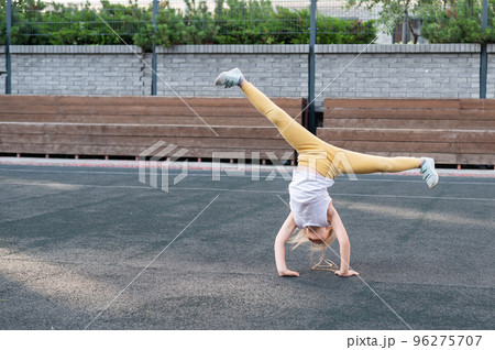 Caucasian girl makes a cartwheel on the sports field outdoors. Caucasian girl makes a cartwheel on the sports field outdoors. 96275707