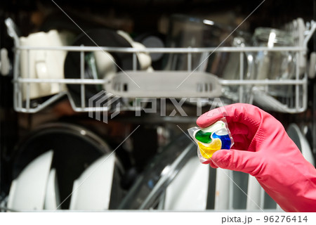 Dishwasher Detergents in hands. hands in pink golvs holds dishwasher gel capsules. Capsule for the dishwasher. Brilliant cleanliness. Dishwasher Detergents in hands. hands in pink golvs holds dishwasher gel capsules. Capsule for the dishwasher. Brilliant cleanliness. 96276414