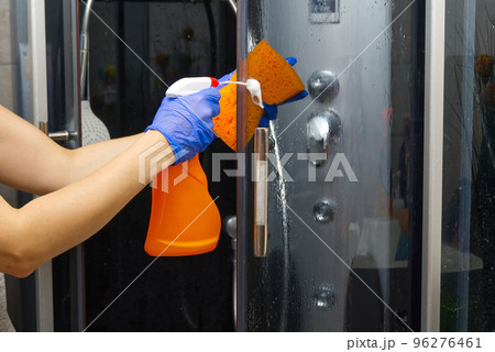 Cleaning of shower steam cabins from calcium deposits. Cleaning in the bathroom. hand in gloves with rag and detergent washing shower and glass 96276461