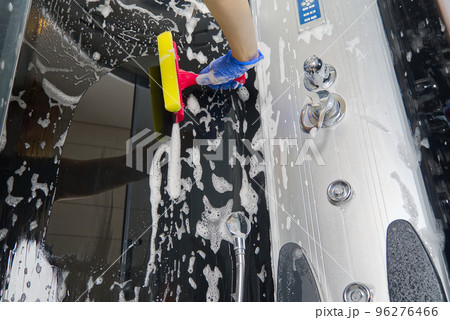 Cleaning of shower steam cabins from calcium deposits. Cleaning in the bathroom. hand in gloves with rag and detergent washing shower and glass 96276466