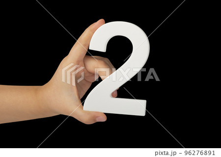Close-up hand holding a white number 2 on a black background. Number two isolate on black background in child's hand. Close-up hand holding a white number 2 on a black background. Number two isolate on black background in child's hand. 96276891