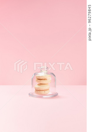 Two vanilla macarons lie in a candy jar on a pink background. 96279845