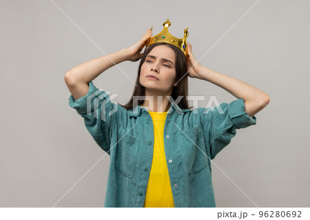 Ambitious woman in golden crown looking with arrogance away, declaring his authority, superior privileged status, wearing casual style jacket. Indoor studio shot isolated on gray background. 96280692