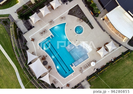 Aerial shot of green lawn, swimming pool, lounge area near beautiful mansion in the courtyard in the summertime. Aerial shot of green lawn, swimming pool, lounge area near beautiful mansion in the courtyard in the summertime. 96280855