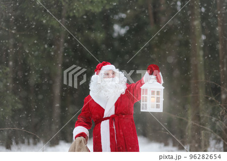 Santa Claus with bag of Christmas gifts is walking through snowy forest. Animator or parent in Santa Claus costume is rushing to a holiday for children. St. Nicholas Day. Santa Claus with bag of Christmas gifts is walking through snowy forest. Animator or parent in Santa Claus costume is rushing to a holiday for children. St. Nicholas Day. 96282654