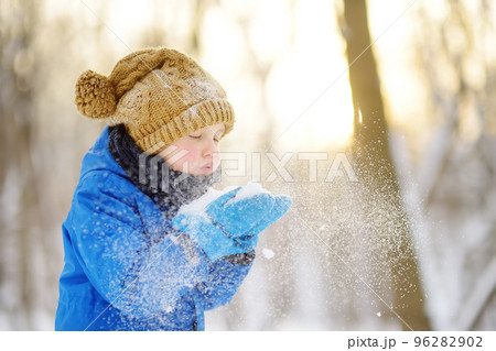Little boy blowing snow from his hands. Child enjoy walking in the park on snowy day. Baby having fun during snowfall. Outdoor winter activities for kids. Little boy blowing snow from his hands. Child enjoy walking in the park on snowy day. Baby having fun during snowfall. Outdoor winter activities for kids. 96282902