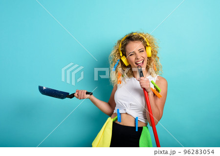 Funny housewife use broom like a rock microphone. cyan background Funny housewife use broom like a rock microphone. cyan background 96283054