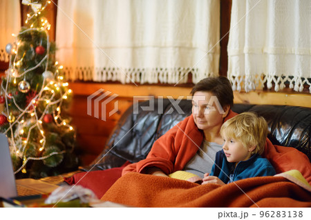 Young grandmother and cute grandchild are sitting on sofa in mountain chalet and watching Christmas movie together. Family leisure during Xmas. Winter holidays on mountain chalet Young grandmother and cute grandchild are sitting on sofa in mountain chalet and watching Christmas movie together. Family leisure during Xmas. Winter holidays on mountain chalet 96283138