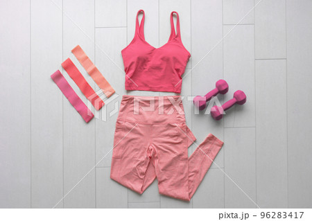 Fitness clothes flat lay workout at home with resistance bands and dumbbell weights. Pink athleisure fashion clothing top view on white wood floor 96283417