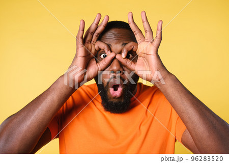 Man do glass with hands. wondered and shocked expression. yellow background Man do glass with hands. wondered and shocked expression. yellow background 96283520