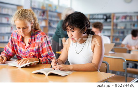 Two schoolgirls preparing for lesson with books in school library Two schoolgirls preparing for lesson with books in school library 96284436