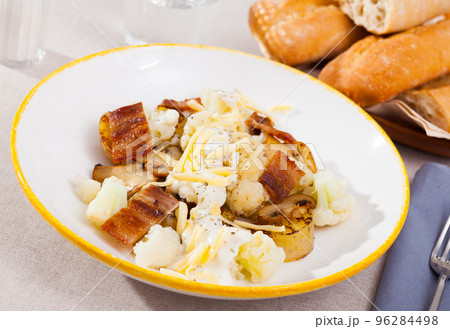 Tasty baked cauliflower with bacon, potatoes with cheese sauce served at plate 96284498