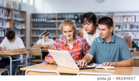 Smiling teenage boy and girls using laptop at library, watching videos 96284637
