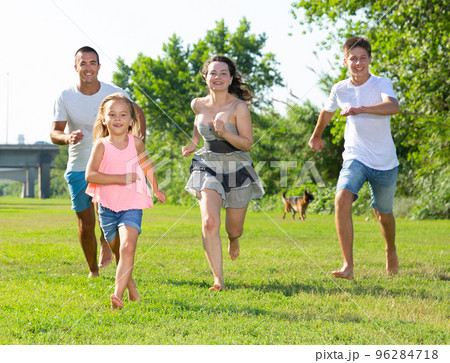 Happy family of four running on grass at summer park 96284718