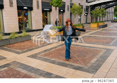 Full length of happy excited young woman in hat dancing and having fun with transparent umbrella on beautiful city street, enjoying rainy weather outdoors. Concept of female lifestyle at autumn season Full length of happy excited young woman in hat dancing and having fun with transparent umbrella on beautiful city street, enjoying rainy weather outdoors. Concept of female lifestyle at autumn season 96287365
