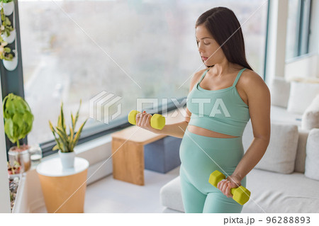 Pregnancy fitness. Pregnant woman home workout fitness strength training exercise with dumbbell weights. Body workout arm curls showing of belly and arms. 2nd and 3rd trimester workouts 96288893