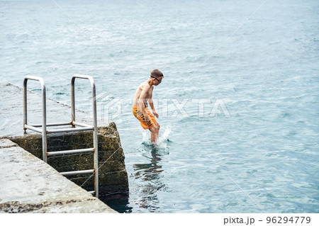 Moments of schoolboy jumping from stone pier with ladder into sea doing tricks in combined image sequence Moments of schoolboy jumping from stone pier with ladder into sea doing tricks in combined image sequence 96294779