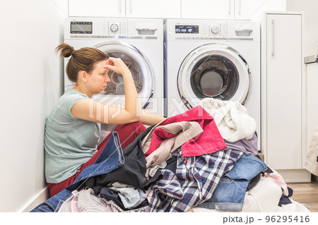 Upset woman in laudry room sitting ona floor with dirty clothes Upset woman in laudry room sitting ona floor with dirty clothes 96295416
