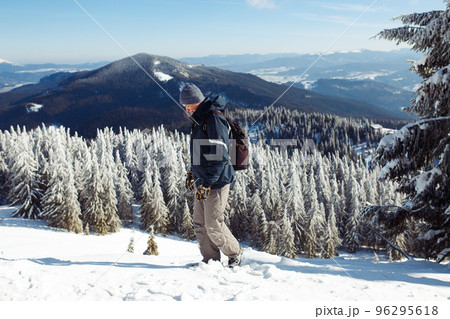 Man with backpack trekking in mountains. Cold weather, snow on hills. Winter hiking. 96295618